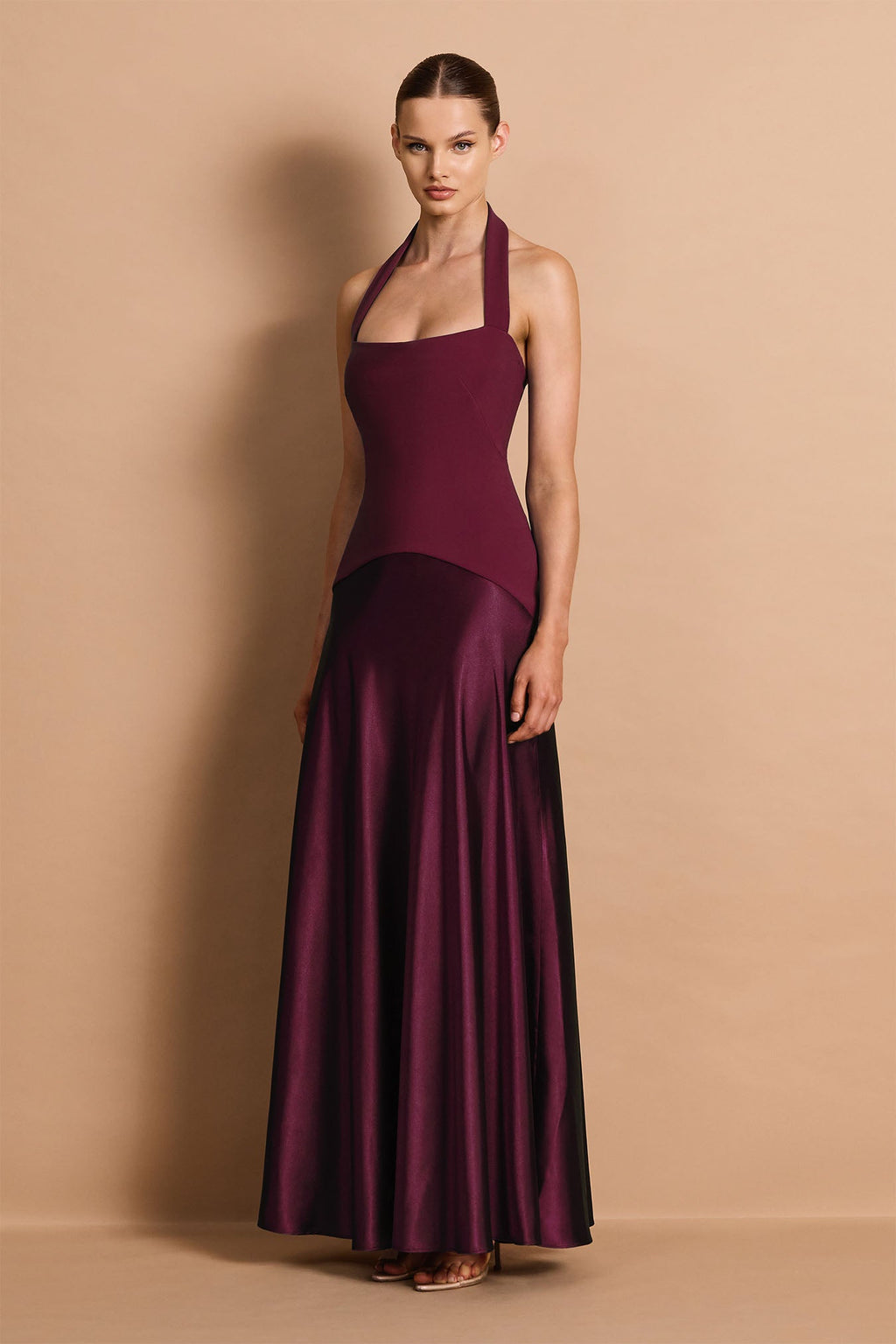 Woman wearing a burgundy halter neck gown against a beige background