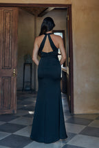Woman in a black dress standing in a doorway with a checkered floor and wooden door.