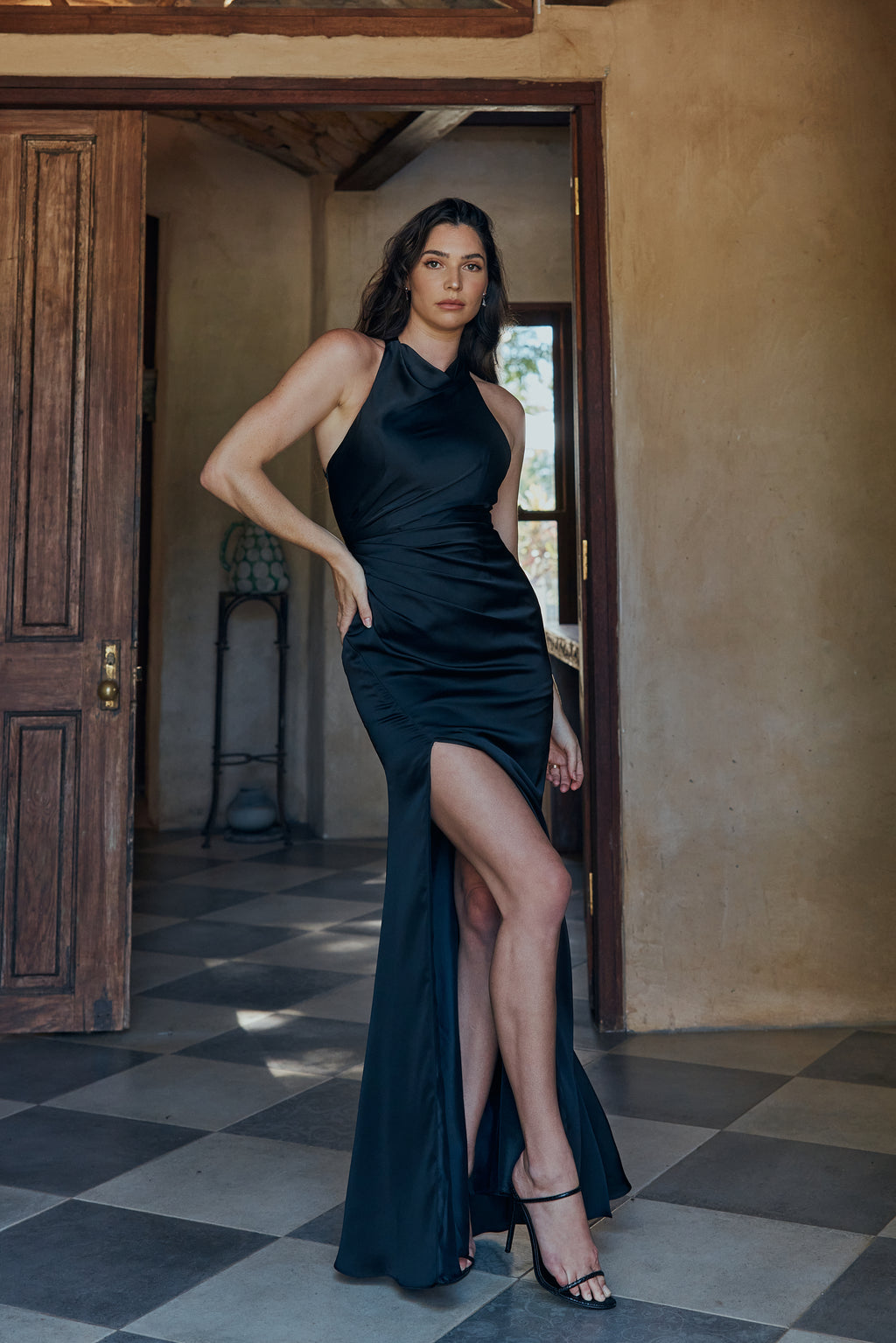 Woman in a black dress standing in a room with a wooden door and tiled floor.