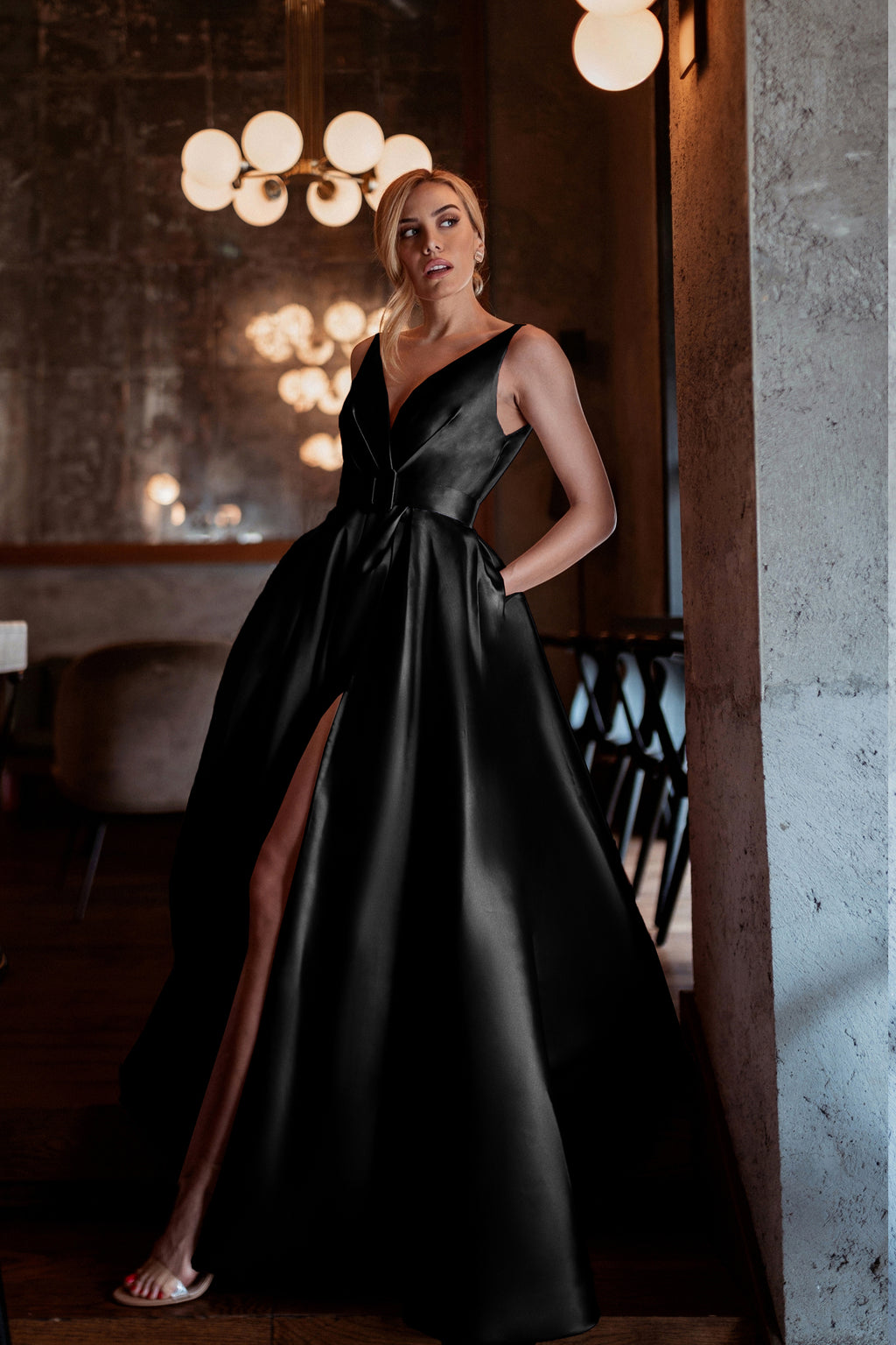 Woman in a black evening gown standing in an elegant interior setting.