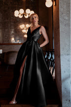 Woman in a black evening gown standing in an elegant interior setting.