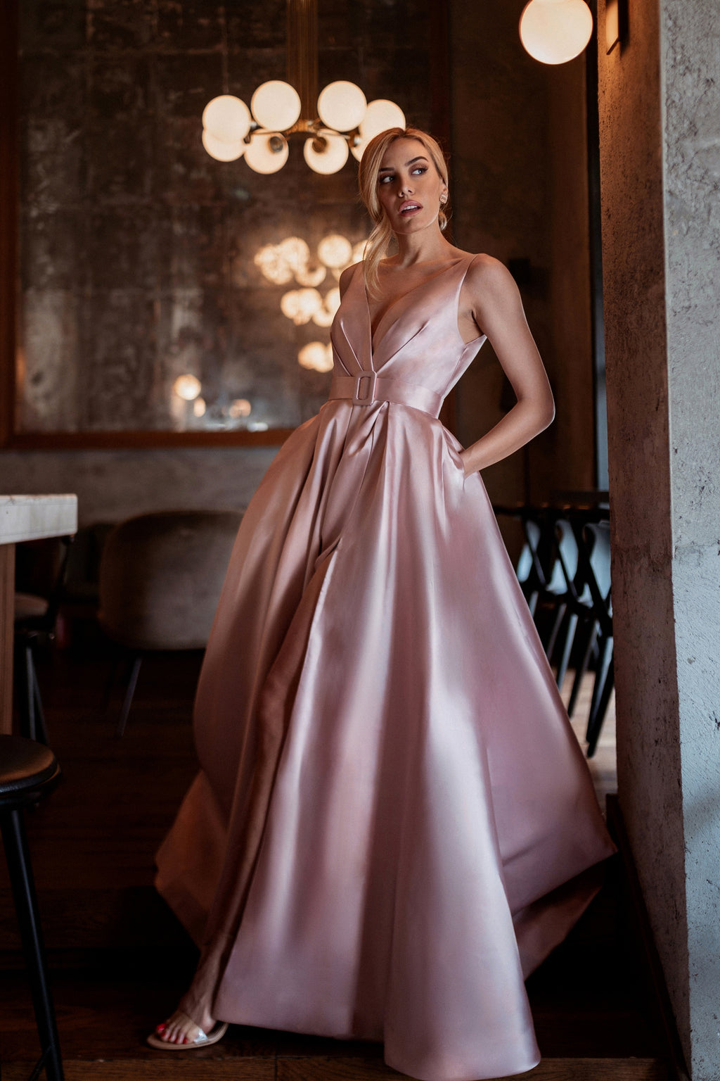 Woman in a pink gown standing in an indoor setting with warm lighting.