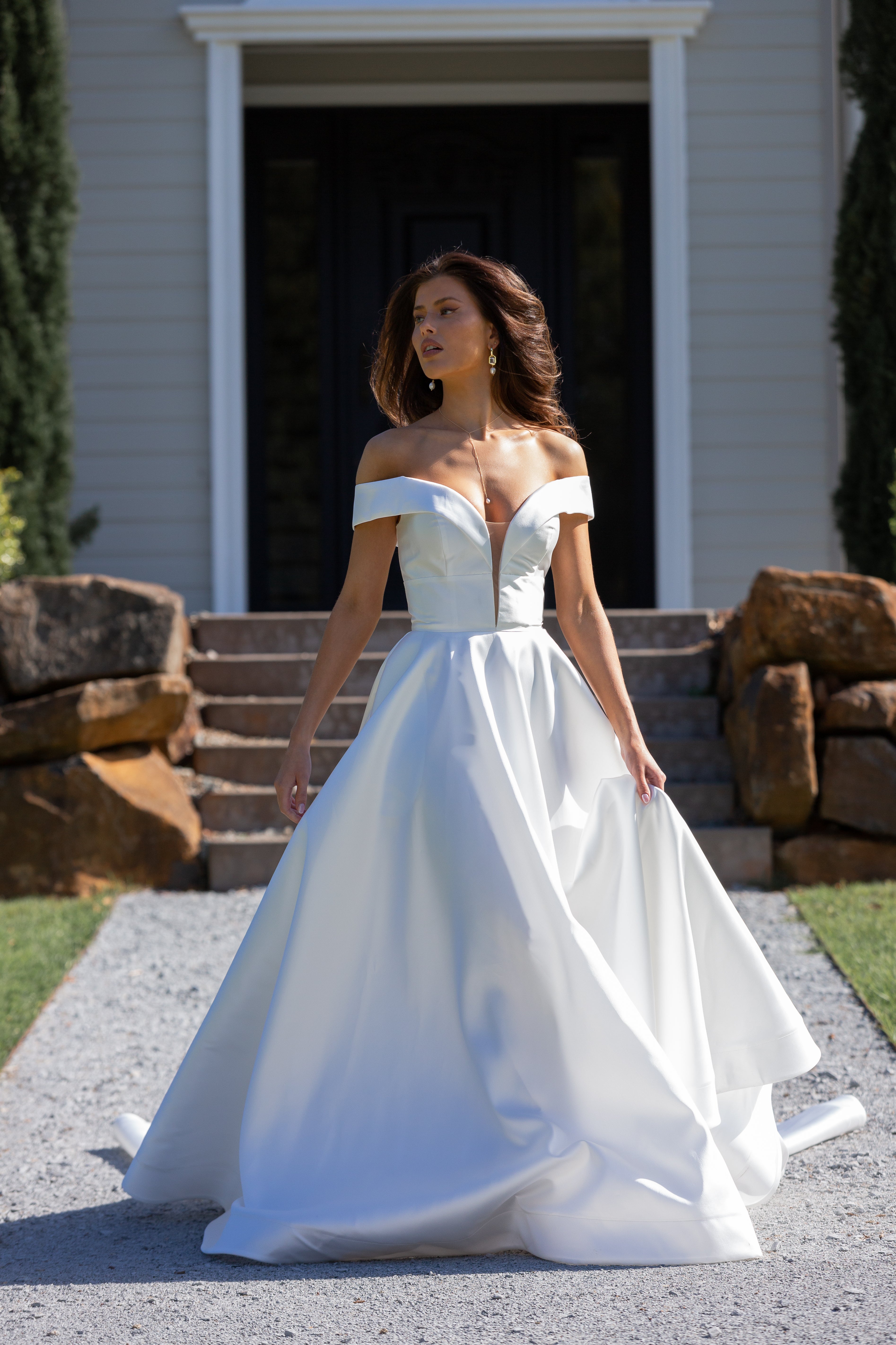 Woman in a white off-shoulder wedding dress standing outdoors.