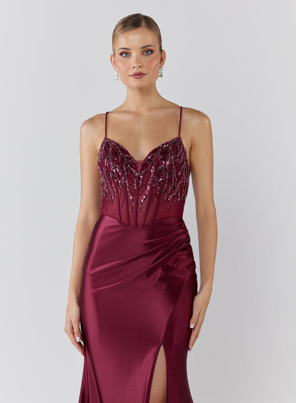 Woman wearing a burgundy evening gown with beaded top on a white background