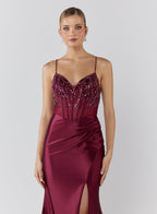 Woman wearing a burgundy evening gown with beaded top on a white background