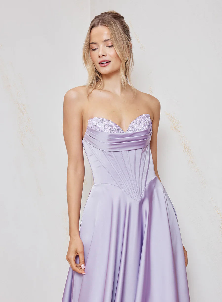 Woman wearing a strapless lavender gown with lace detailing against a light background