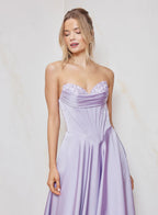Woman wearing a strapless lavender gown with lace detailing against a light background