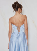 Woman wearing a light blue dress with a lace-up back against a neutral background