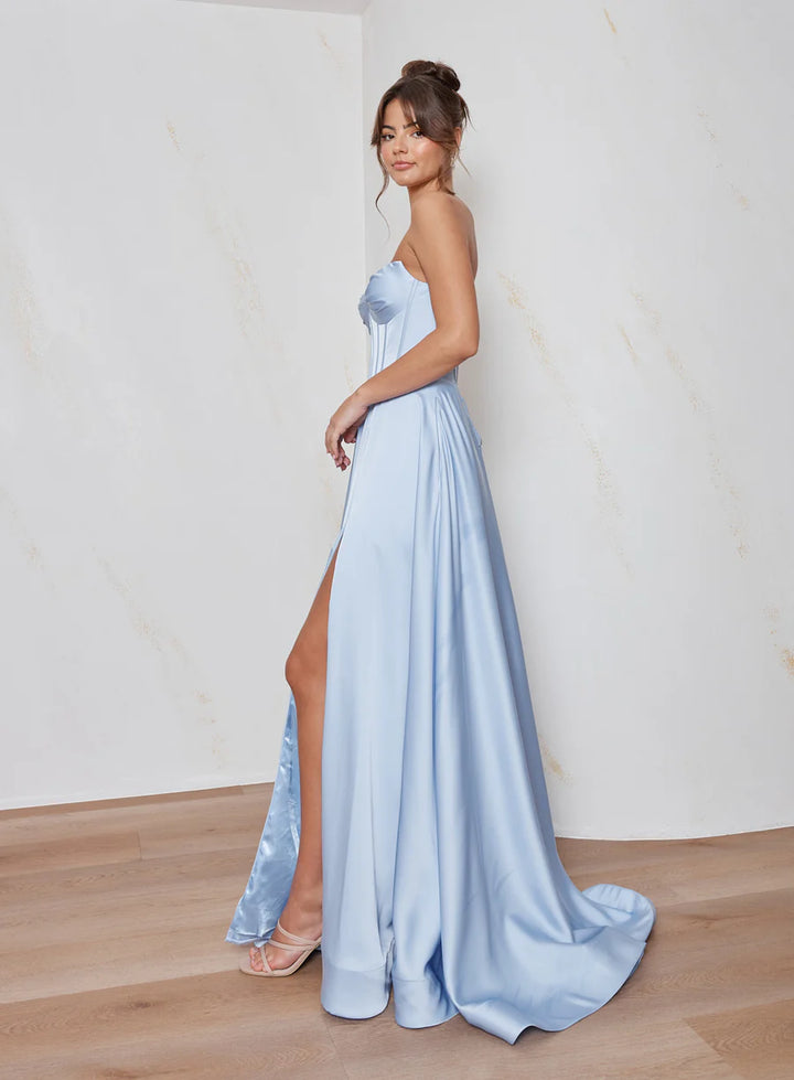 Woman wearing a light blue strapless gown with a high slit on a plain background