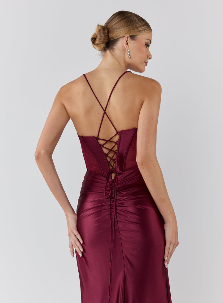 Woman wearing a burgundy evening gown with a criss-cross back design on a light gray background