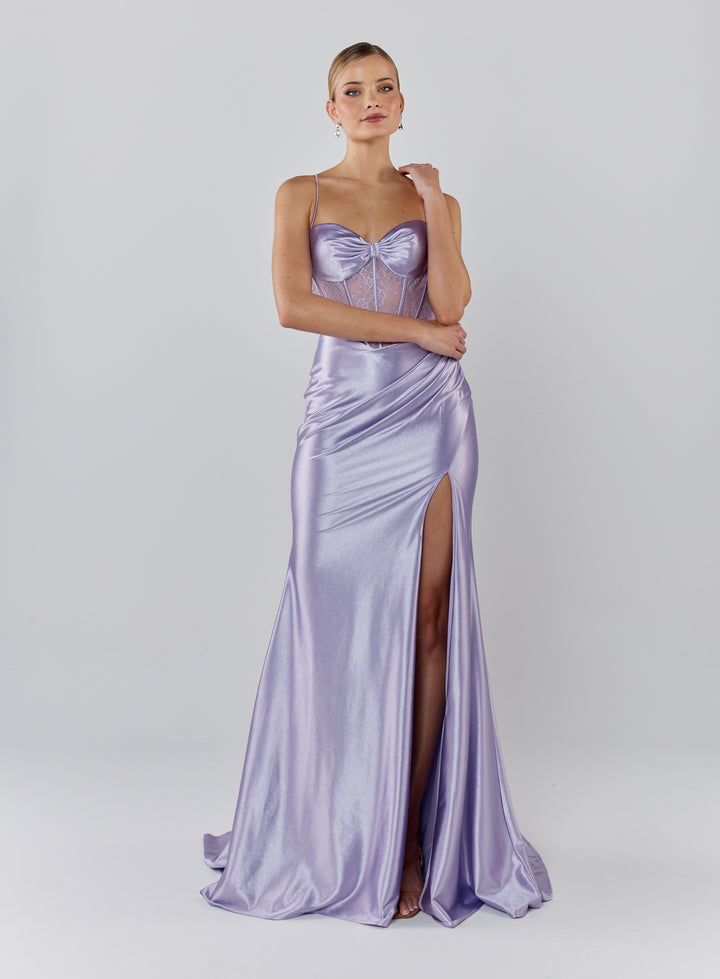 Woman wearing a lavender evening gown with a bow detail on a white background