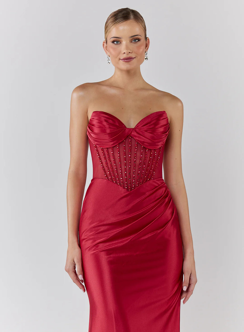 Woman wearing a red strapless gown with beaded details on a white background