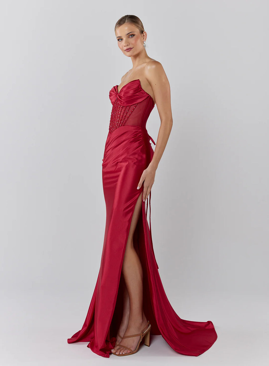 Woman wearing a red strapless gown with a high slit on a white background