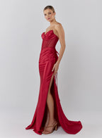Woman wearing a red strapless gown with a high slit on a white background