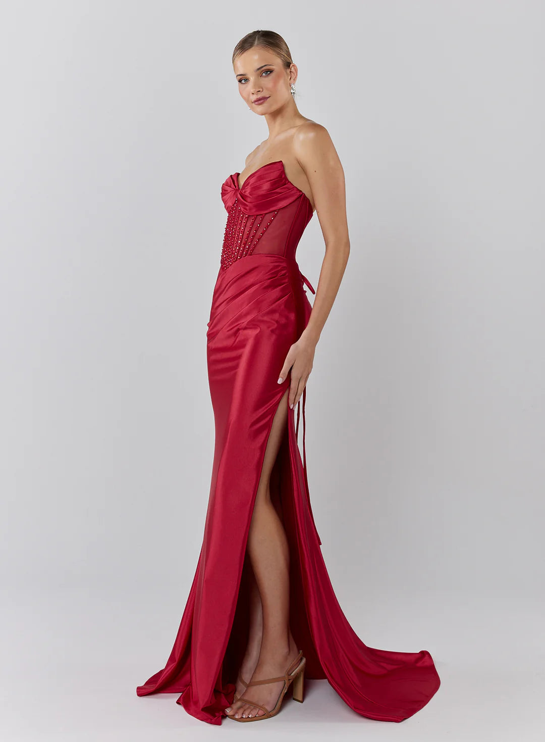 Woman wearing a red strapless gown with a high slit on a white background