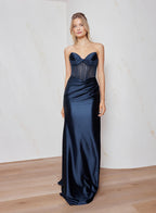Woman wearing a navy blue strapless gown against a plain background