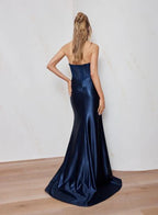 Woman wearing a navy blue strapless gown against a plain background