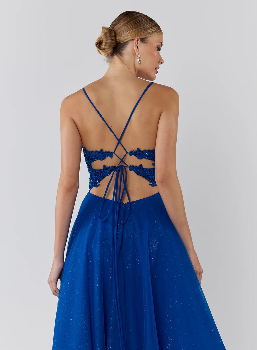Woman wearing a blue dress with a lace-up back on a plain background