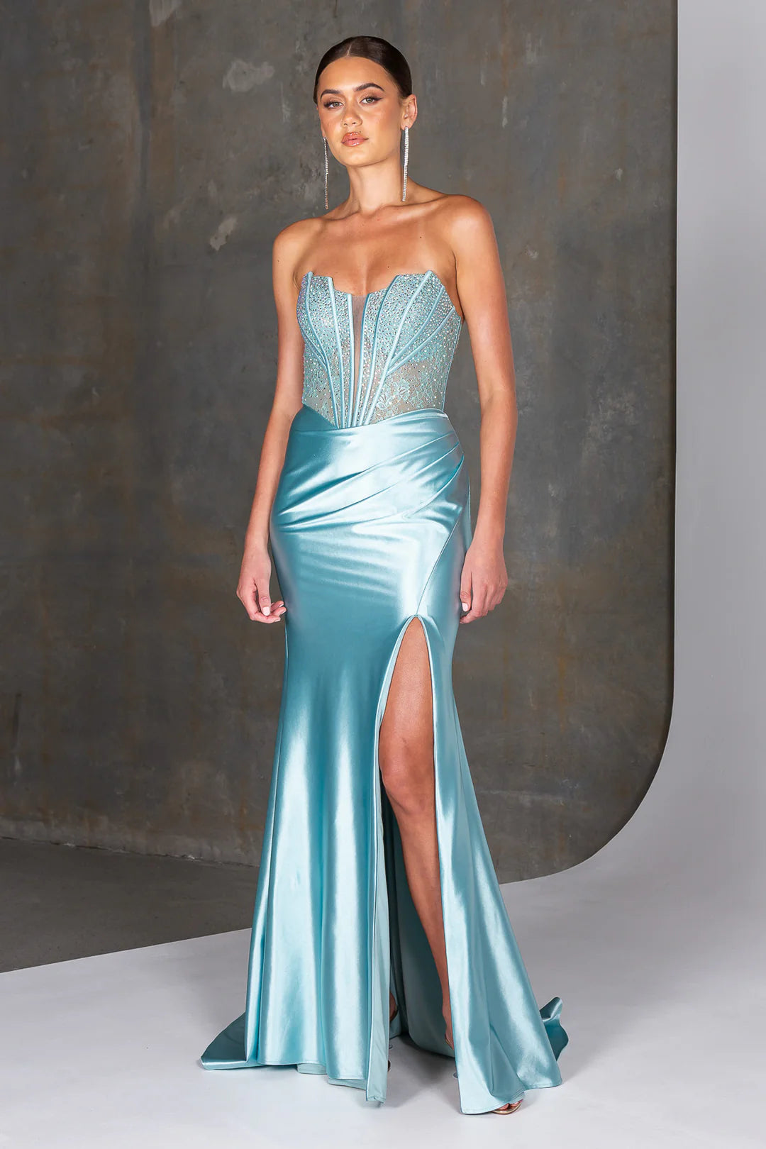 Woman wearing a light blue evening gown with a high slit on a neutral background