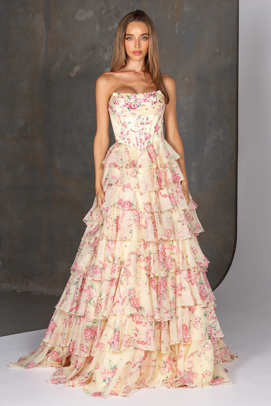 Woman wearing a strapless floral gown with ruffled layers against a neutral background