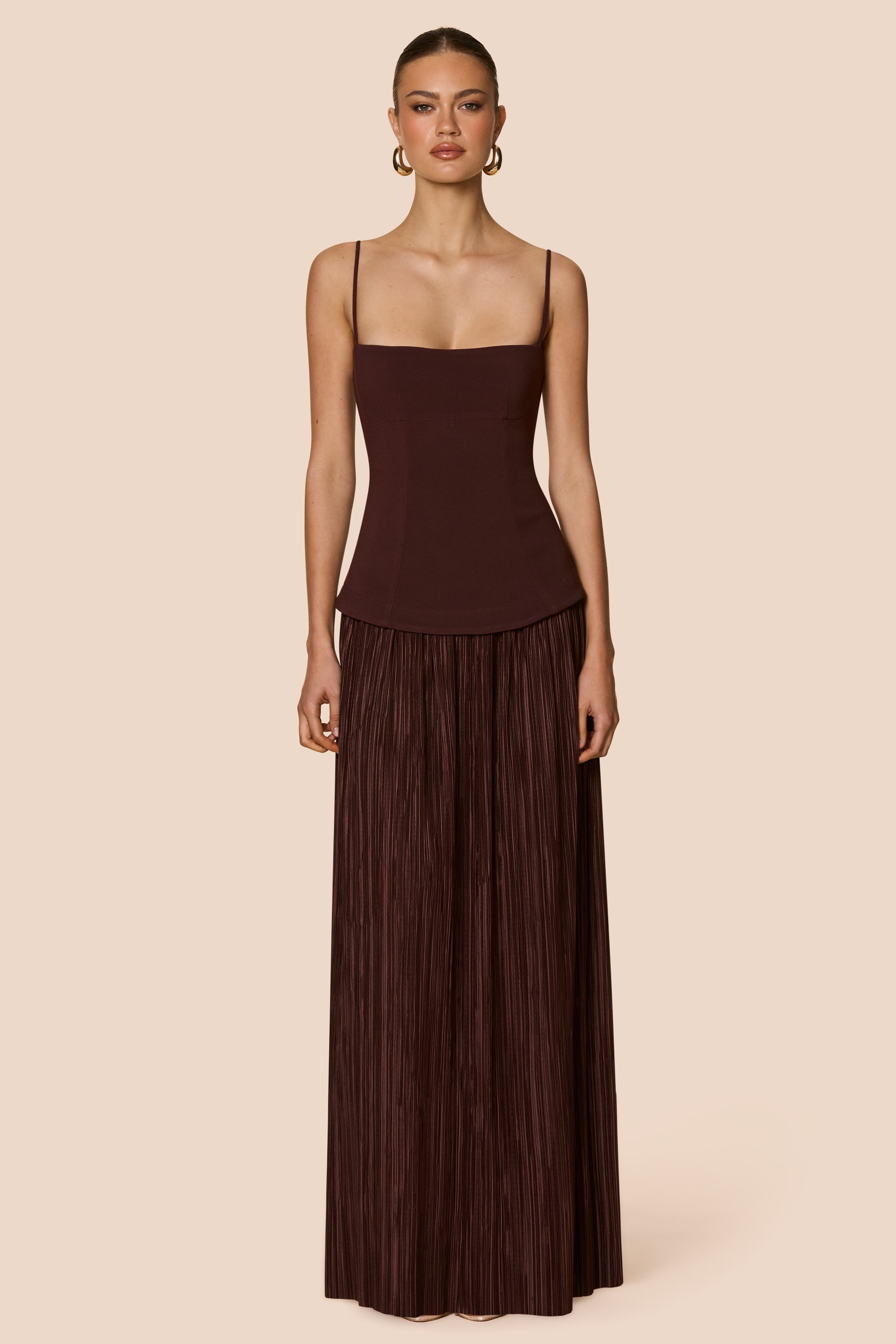 Woman wearing a brown pleated dress against a beige background
