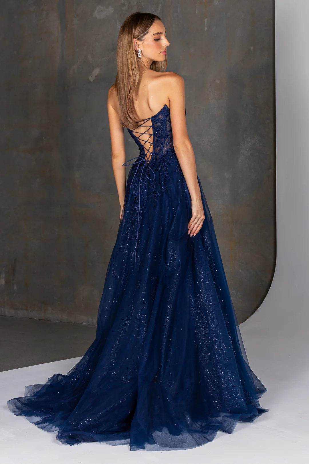 Navy blue evening gown with intricate lace details on a neutral background
