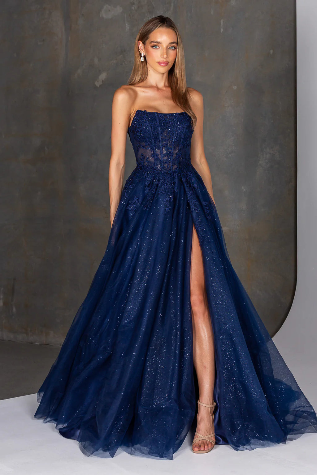 Woman wearing a navy blue evening gown with a slit on a gray background