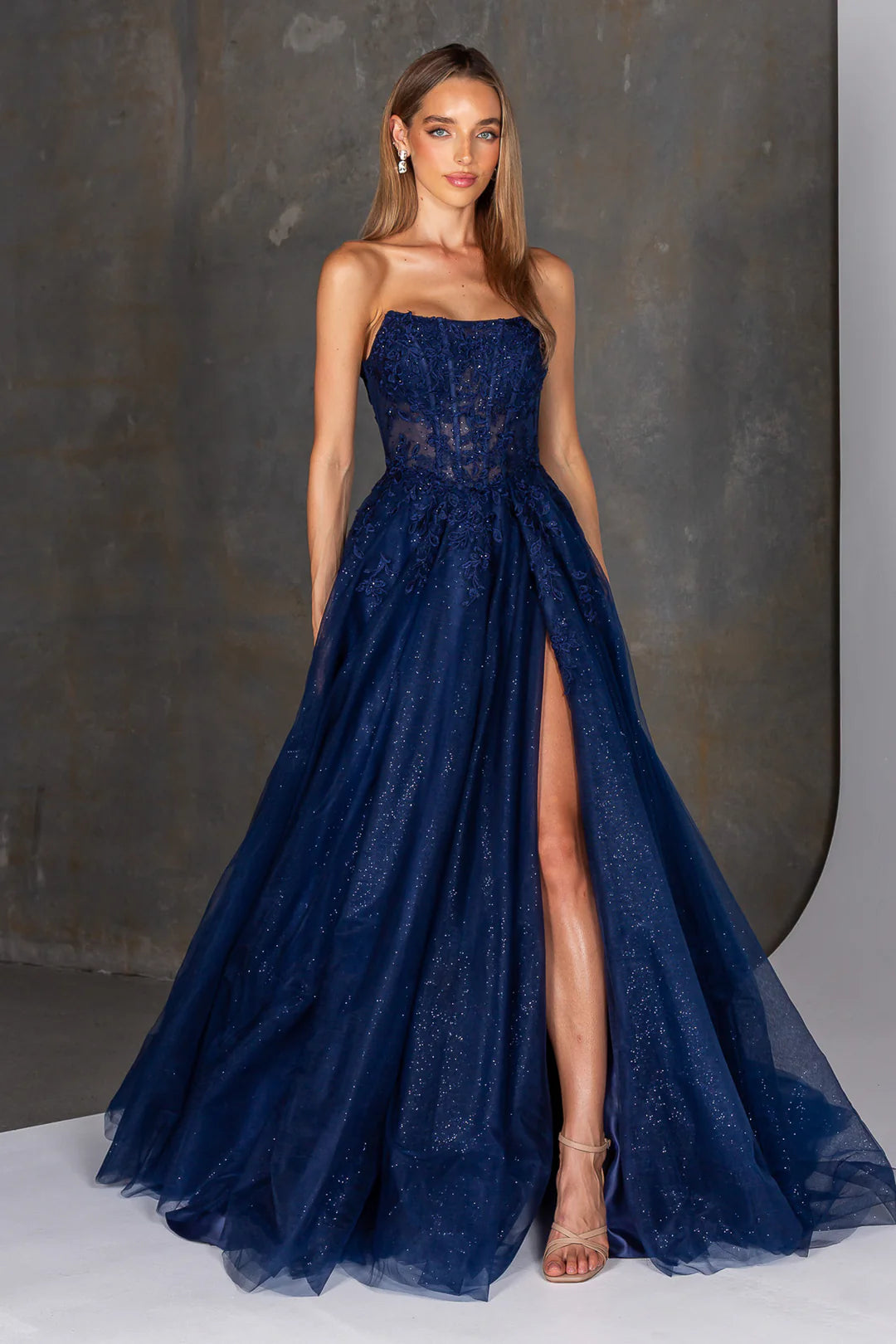 Woman wearing a navy blue evening gown with a slit on a gray background