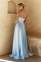 Woman in a light blue dress standing against a beige wall.