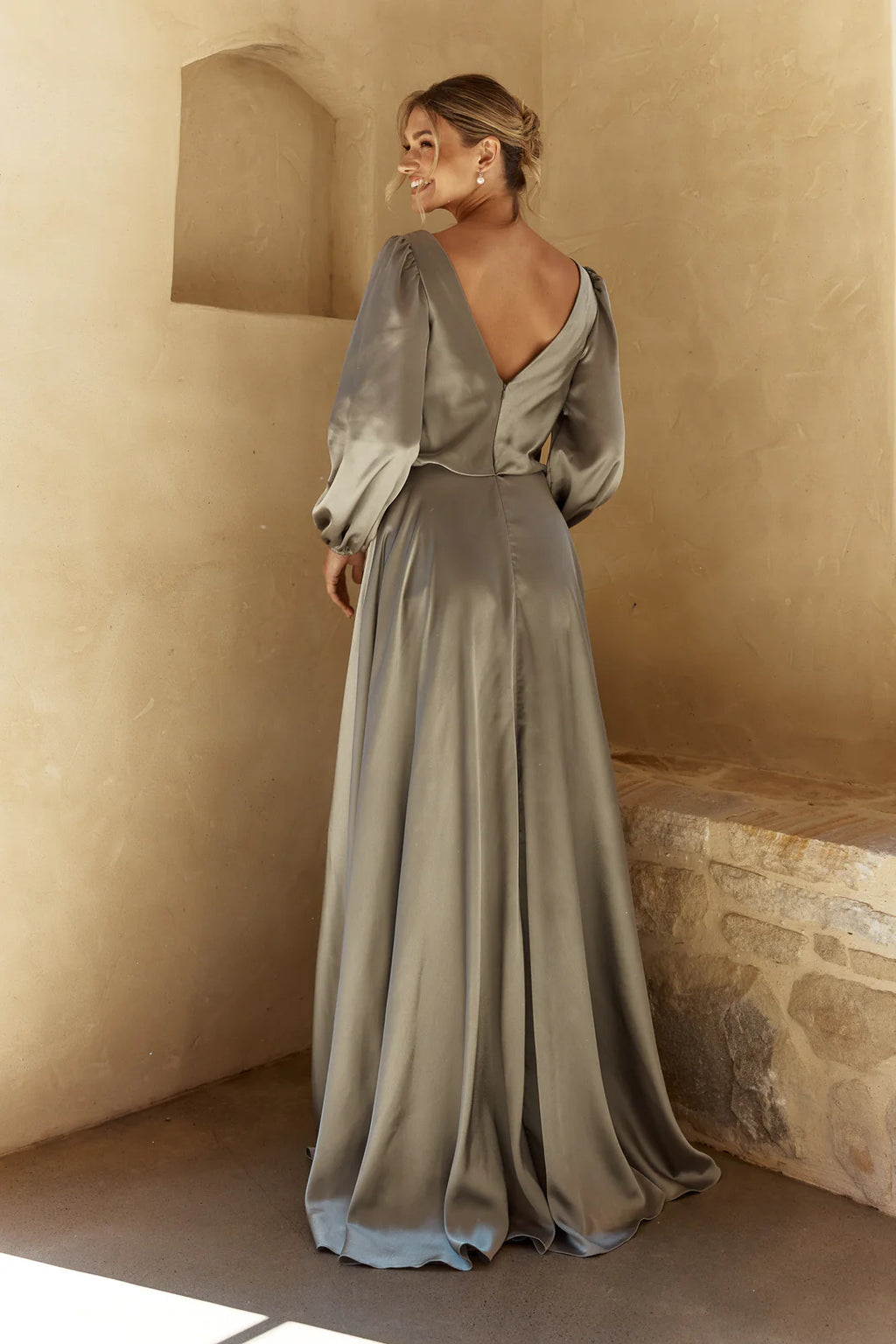Woman in a long, flowing dress standing against a beige wall.
