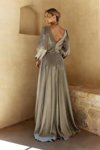 Woman in a long, flowing dress standing against a beige wall.