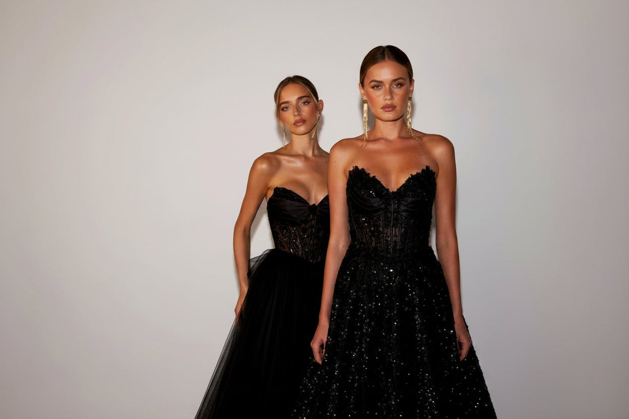 Two women wearing black strapless dresses against a plain background