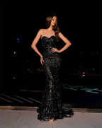 Woman in a black strapless gown standing outdoors at night.