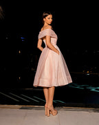 Woman in a pink off-shoulder dress standing against a dark background