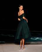 Woman in a dark green off-shoulder dress standing against a black background