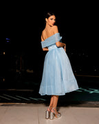 Woman in a light blue off-shoulder dress standing against a dark background