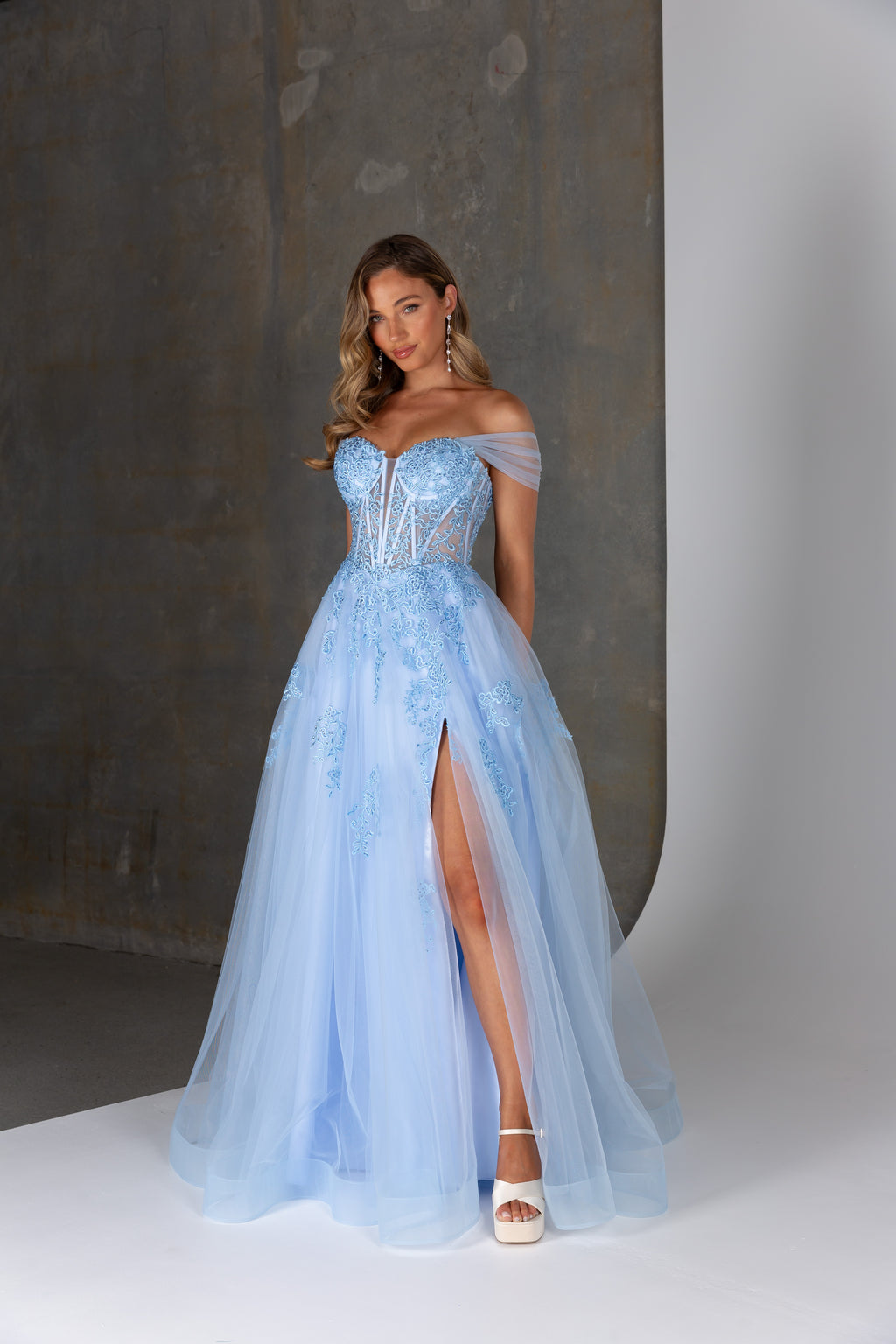 Woman wearing a light blue evening gown with a high slit on a neutral background