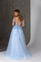 Woman wearing a light blue evening gown with a lace-up back against a neutral background