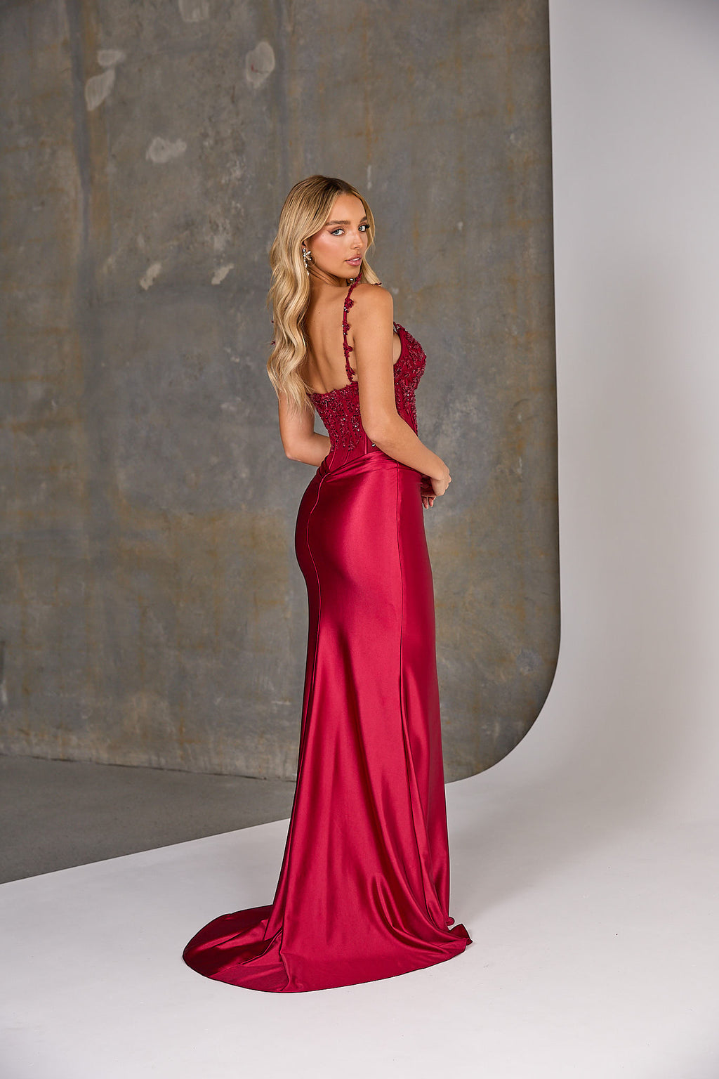 Woman in a red evening gown standing against a neutral background