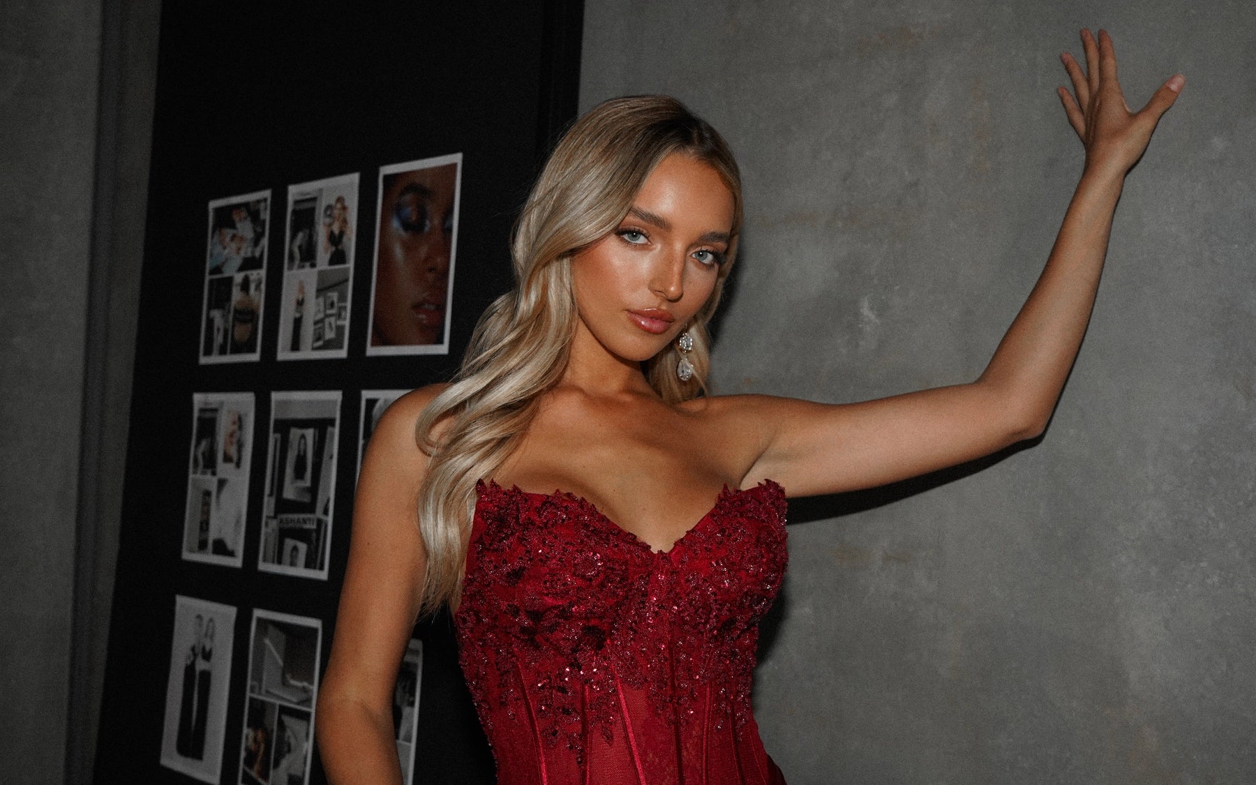 Woman in a red dress posing against a gray wall with framed pictures.