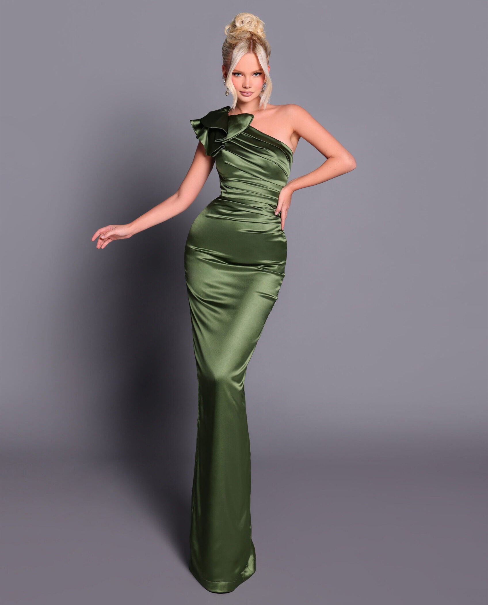 Woman wearing a green satin one-shoulder gown against a gray background