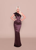Woman wearing a long, dark purple evening gown against a beige background