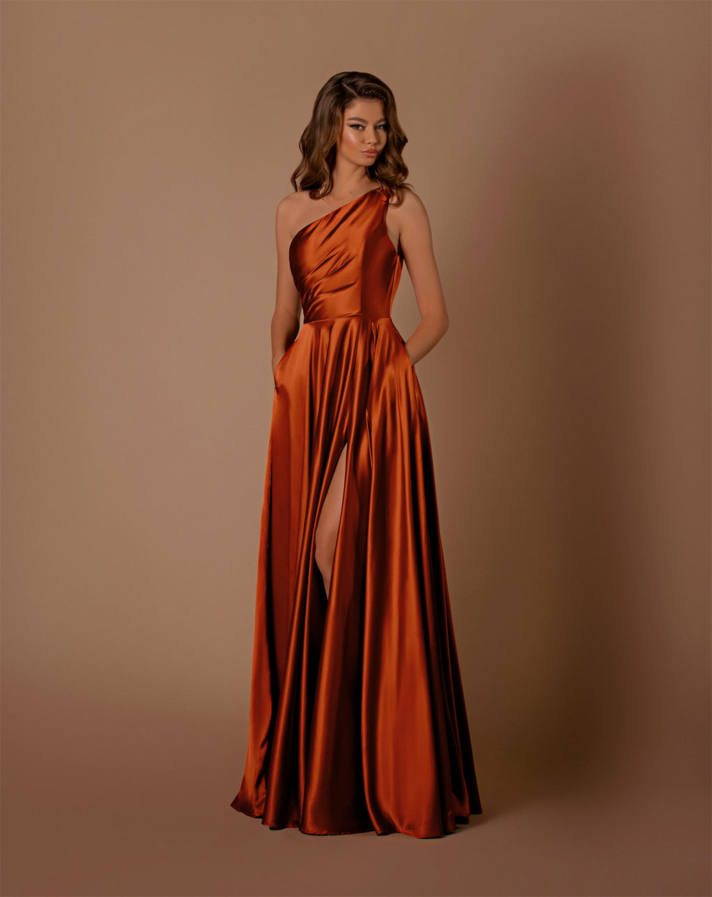 Woman wearing a rust-colored one-shoulder gown with a slit on a brown background