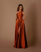 Woman wearing a rust-colored one-shoulder gown with a slit on a brown background