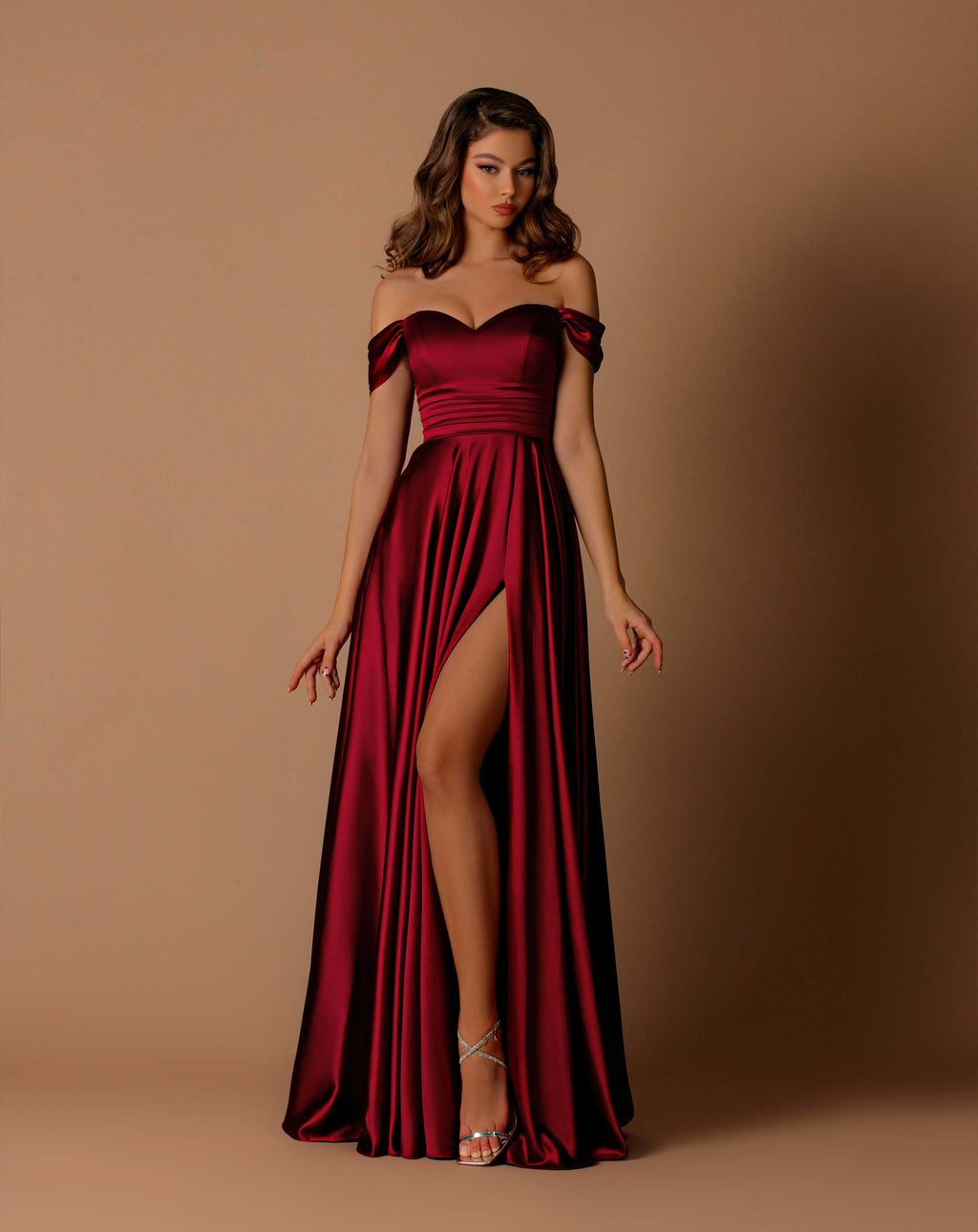 Woman wearing a burgundy off-shoulder gown with a slit on a brown background