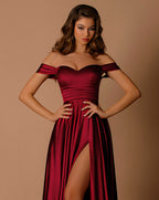 Woman wearing a burgundy off-shoulder dress with a high slit on a beige background