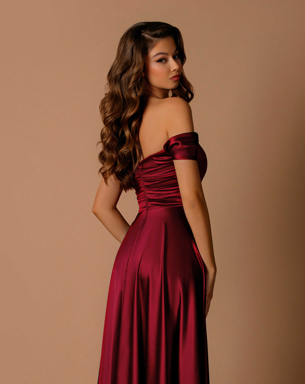 Woman wearing a burgundy off-shoulder dress against a beige background