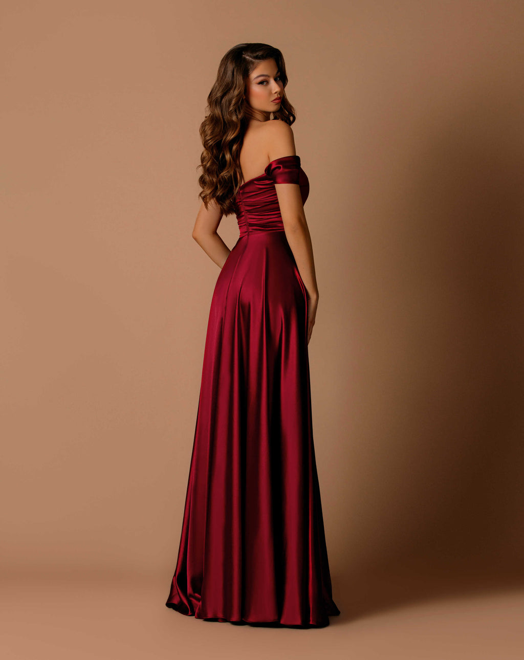 Woman wearing a burgundy off-shoulder gown against a beige background