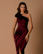 Woman wearing a burgundy one-shoulder dress against a beige background