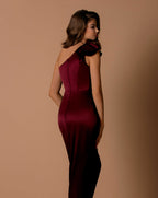 Woman wearing a burgundy one-shoulder dress against a brown background